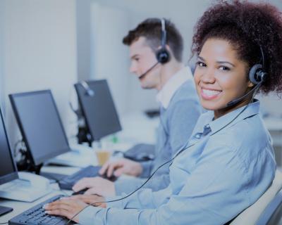 Two people at their desks in front of their computers wearing headphones